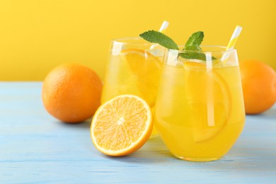 Photo of Refreshing soda water with orange slices in glasses, mint and fresh fruits on light blue wooden table, closeup