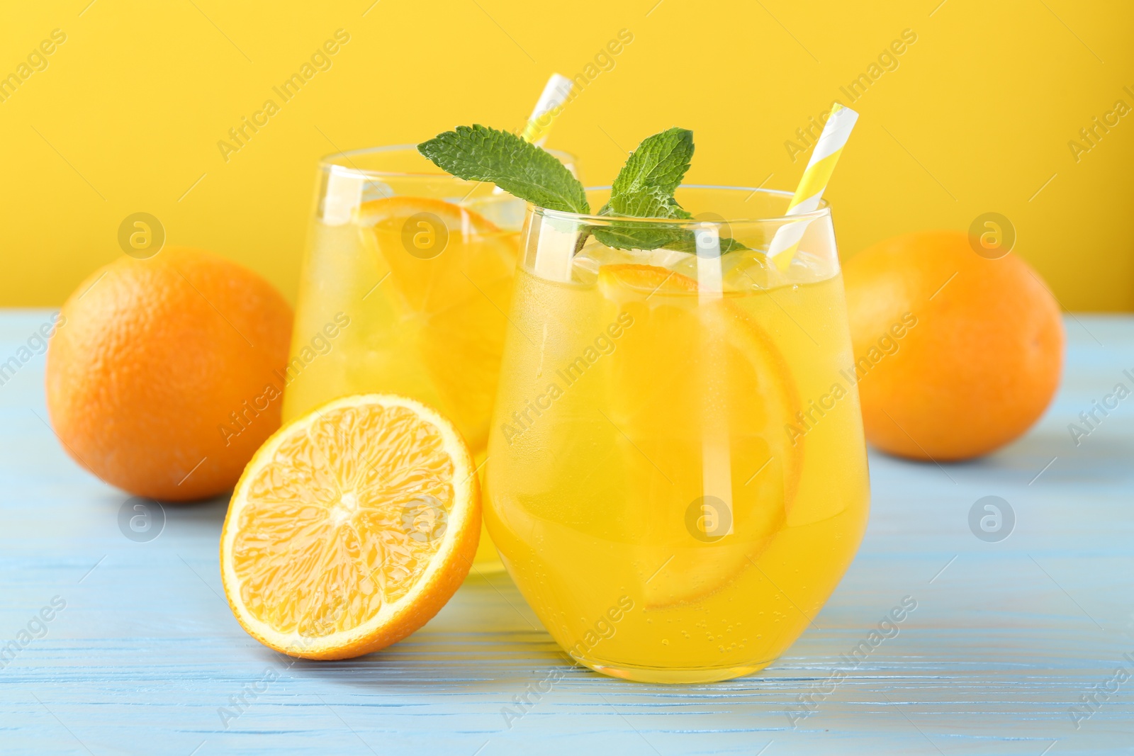Photo of Refreshing soda water with orange slices in glasses, mint and fresh fruits on light blue wooden table, closeup
