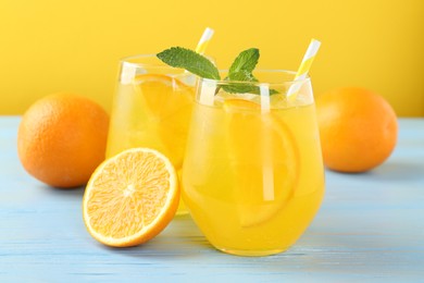 Photo of Refreshing soda water with orange slices in glasses, mint and fresh fruits on light blue wooden table, closeup