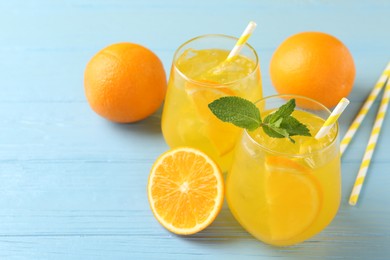 Photo of Refreshing soda water with orange slices in glasses, mint, fresh fruits and straws on light blue wooden table, closeup. Space for text