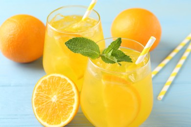 Photo of Refreshing soda water with orange slices in glasses, mint, fresh fruits and straws on light blue wooden table, closeup