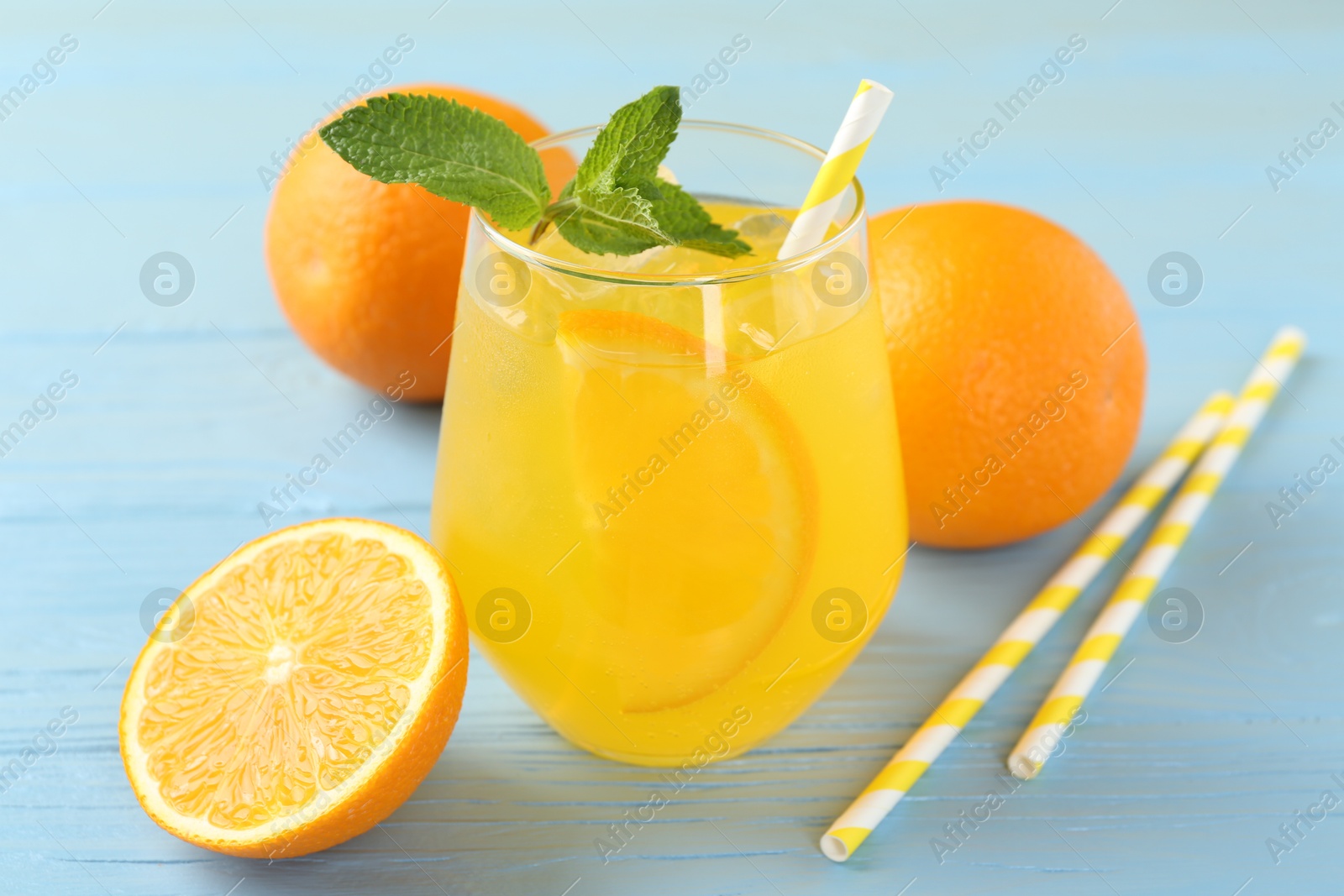 Photo of Refreshing soda water with orange slice in glass, mint, fresh fruits and straws on light blue wooden table, closeup