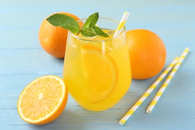 Photo of Refreshing soda water with orange slice in glass, mint, fresh fruits and straws on light blue wooden table, closeup