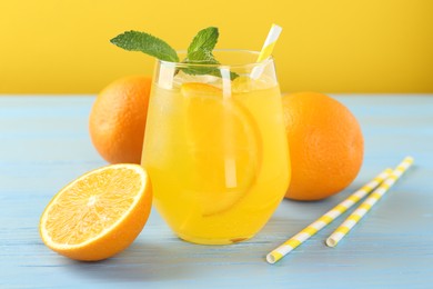 Photo of Refreshing soda water with orange slice in glass, mint, fresh fruits and straws on light blue wooden table, closeup