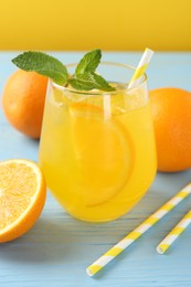 Photo of Refreshing soda water with orange slice in glass, mint, fresh fruits and straws on light blue wooden table, closeup