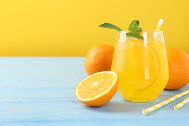 Photo of Refreshing soda water with orange slice in glass, mint, fresh fruits and straws on light blue wooden table, closeup. Space for text