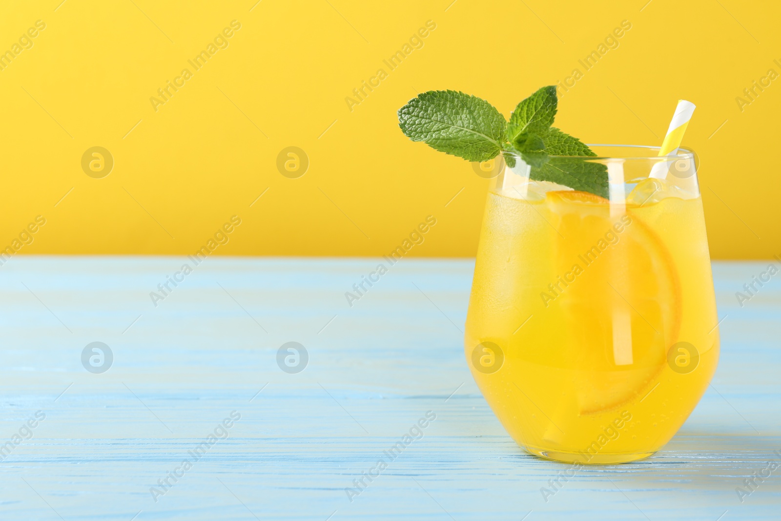 Photo of Refreshing soda water with orange slice in glass and mint on light blue wooden table, closeup. Space for text