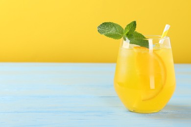 Photo of Refreshing soda water with orange slice in glass and mint on light blue wooden table, closeup. Space for text