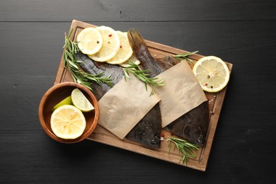 Photo of Fresh raw flounder fish and spices on black wooden table, top view. Seafood