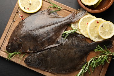 Photo of Fresh raw flounder fish and spices on black wooden table, flat lay. Seafood