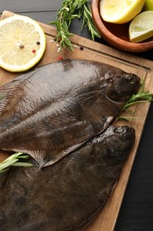 Photo of Fresh raw flounder fish and spices on black wooden table, flat lay. Seafood