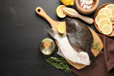 Photo of Seafood. Fresh raw flounder fish, spices and juicer on black wooden table, flat lay. Space for text
