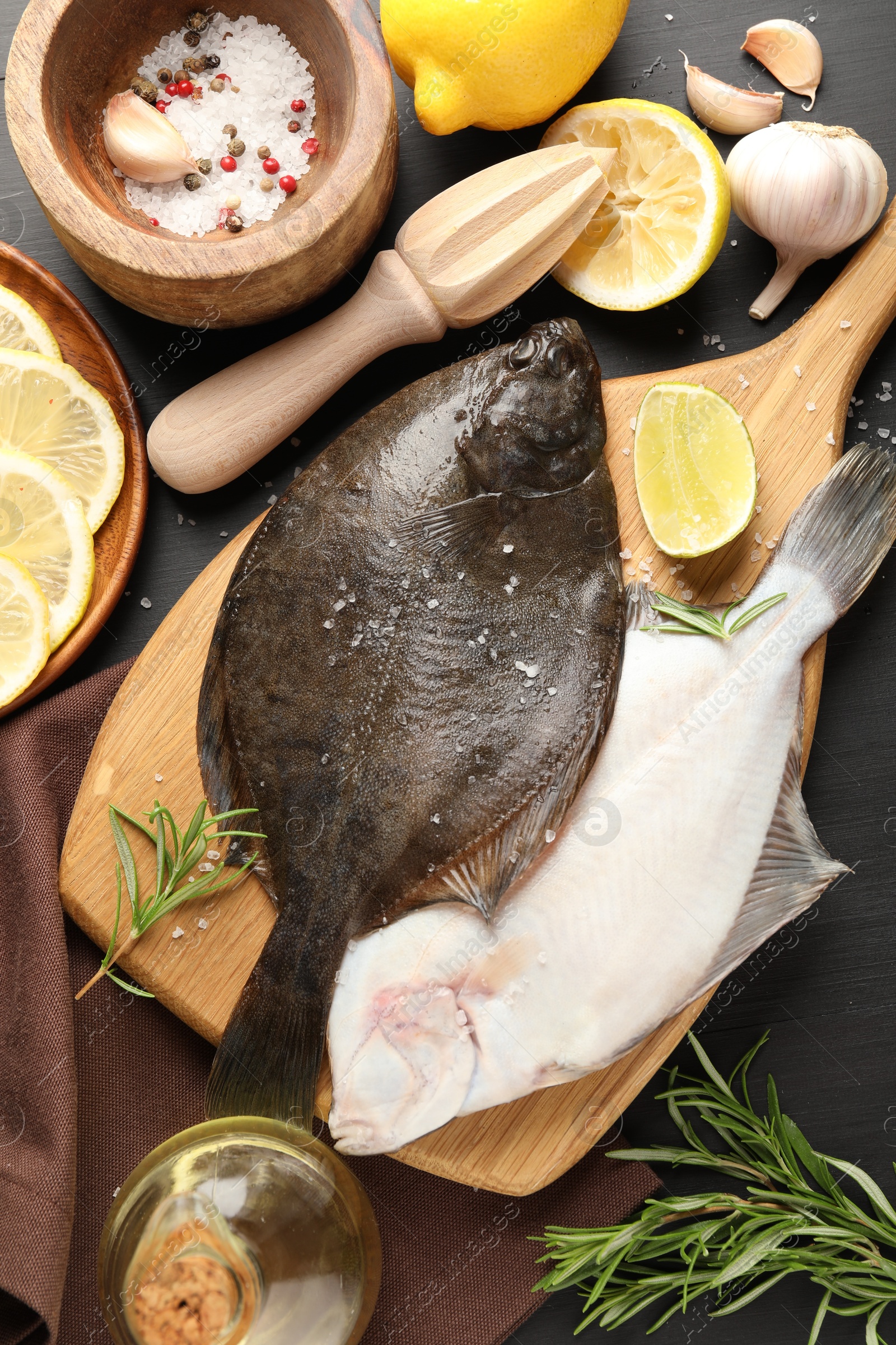 Fresh raw flounder fish, spices and juicer on black wooden table, flat lay. Seafood Photo of Fresh raw flounder fish, spices and juicer on black wooden table, flat lay. Seafood