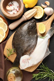 Photo of Fresh raw flounder fish, spices and juicer on black wooden table, flat lay. Seafood