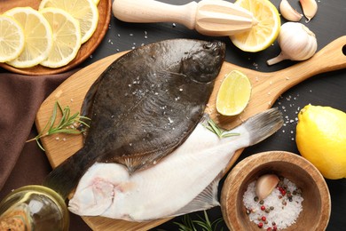 Photo of Fresh raw flounder fish, spices and juicer on black wooden table, flat lay. Seafood