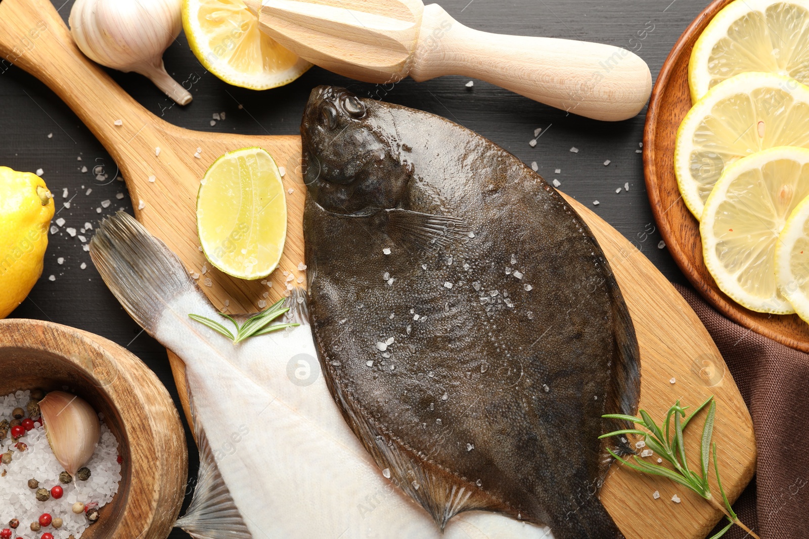 Fresh raw flounder fish, spices and juicer on black wooden table, flat lay. Seafood Photo of Fresh raw flounder fish, spices and juicer on black wooden table, flat lay. Seafood