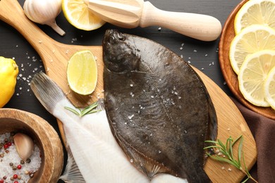 Photo of Fresh raw flounder fish, spices and juicer on black wooden table, flat lay. Seafood