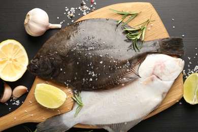Photo of Fresh raw flounder fish and spices on black wooden table, flat lay. Seafood