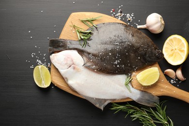 Photo of Fresh raw flounder fish and spices on black wooden table, flat lay. Seafood