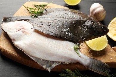 Photo of Fresh raw flounder fish and spices on black wooden table, closeup. Seafood