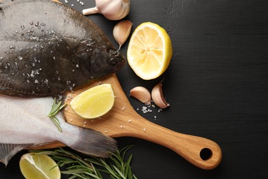 Photo of Seafood. Fresh raw flounder fish and spices on black wooden table, flat lay. Space for text