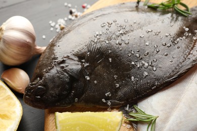 Photo of Fresh raw flounder fish and spices on black wooden table, closeup. Seafood
