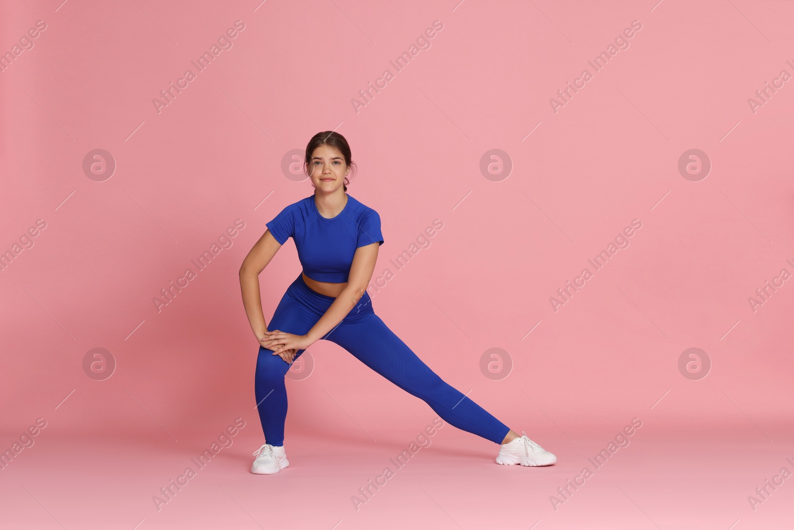 Teenage girl in sportswear stretching on pink background Photo of Teenage girl in sportswear stretching on pink background