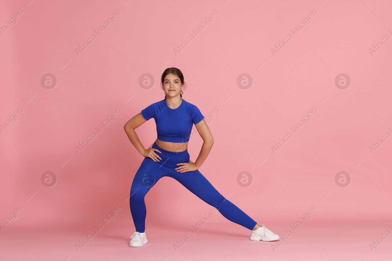 Teenage girl in sportswear stretching on pink background Photo of Teenage girl in sportswear stretching on pink background