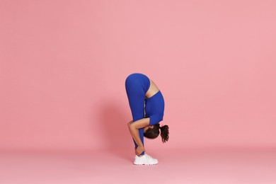 Photo of Teenage girl in sportswear stretching on pink background
