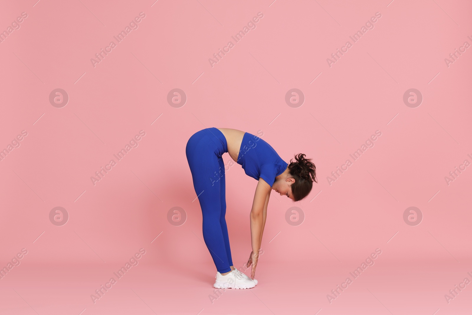 Teenage girl in sportswear stretching on pink background Photo of Teenage girl in sportswear stretching on pink background