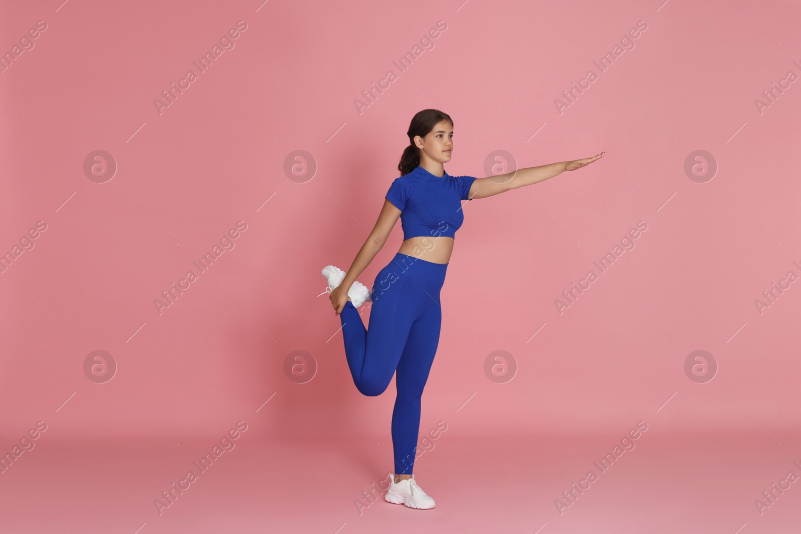 Teenage girl in sportswear stretching on pink background Photo of Teenage girl in sportswear stretching on pink background