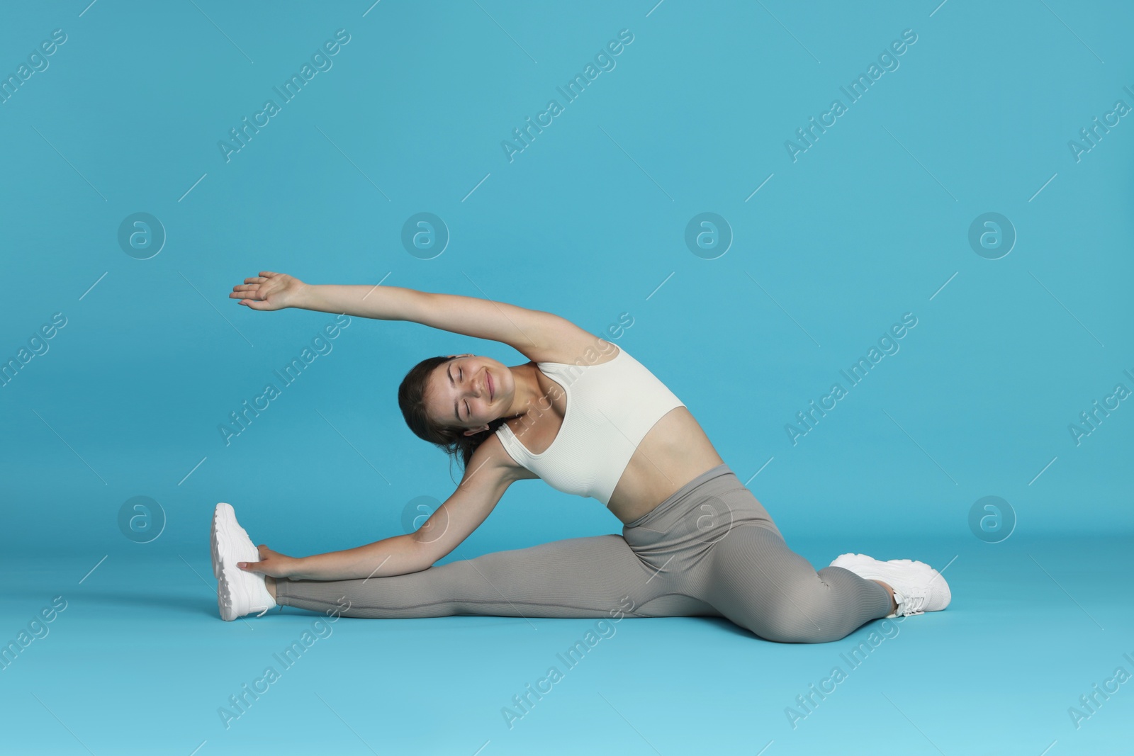 Teenage girl in sportswear stretching on light blue background Photo of Teenage girl in sportswear stretching on light blue background