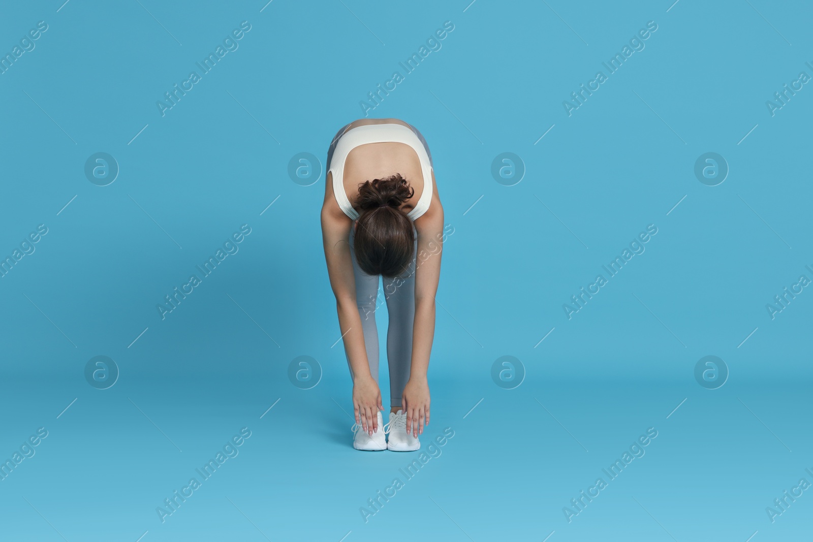 Teenage girl in sportswear stretching on light blue background Photo of Teenage girl in sportswear stretching on light blue background