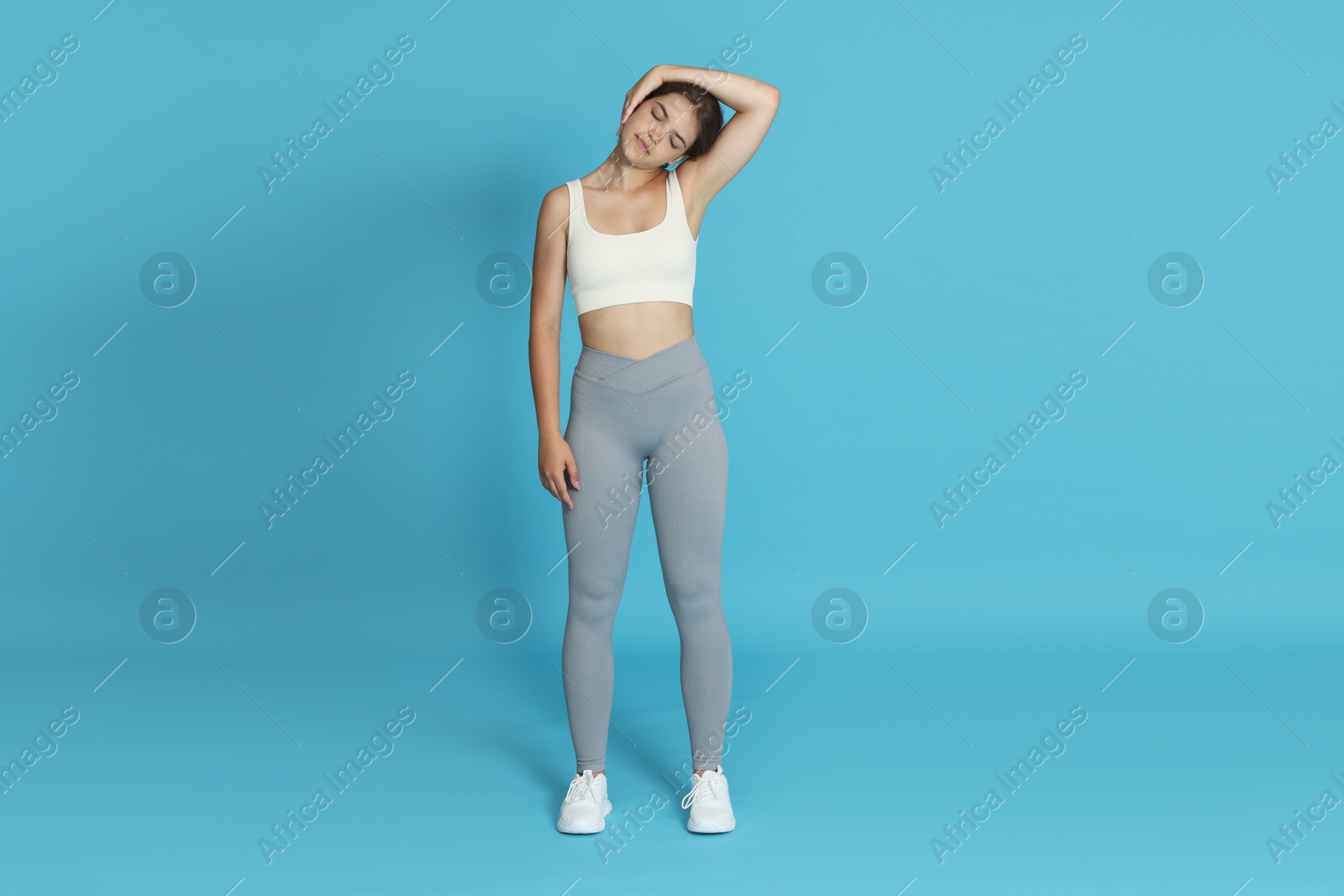 Teenage girl in sportswear stretching on light blue background Photo of Teenage girl in sportswear stretching on light blue background