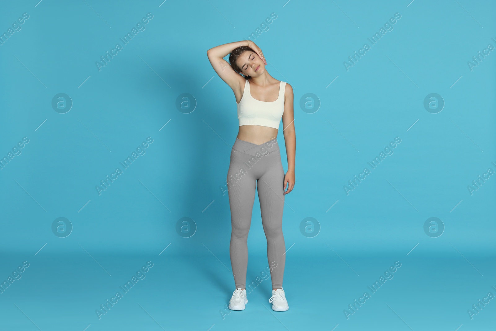 Teenage girl in sportswear stretching on light blue background Photo of Teenage girl in sportswear stretching on light blue background