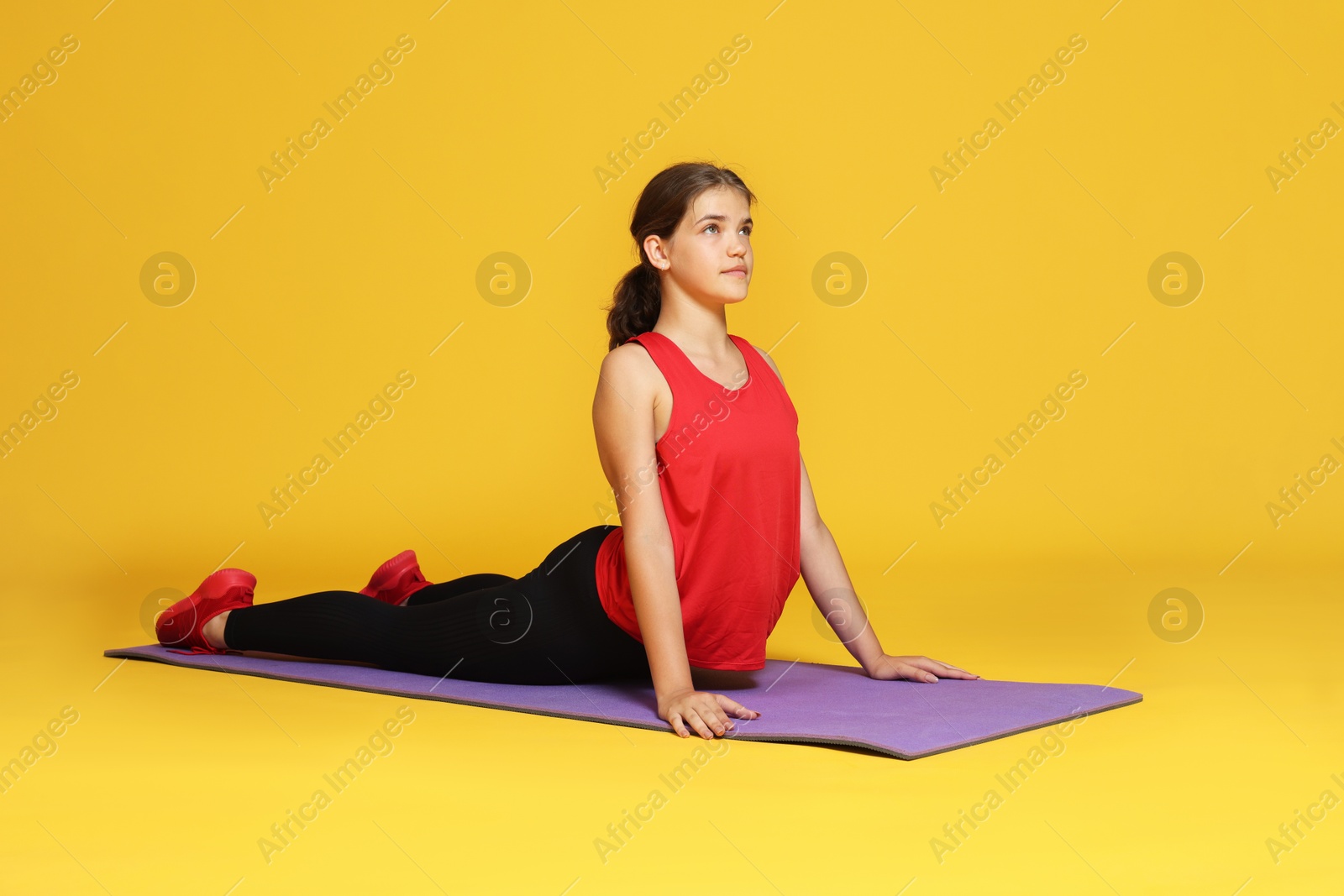 Teenage girl in sportswear stretching on mat against orange background Photo of Teenage girl in sportswear stretching on mat against orange background