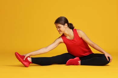 Photo of Teenage girl in sportswear stretching on orange background