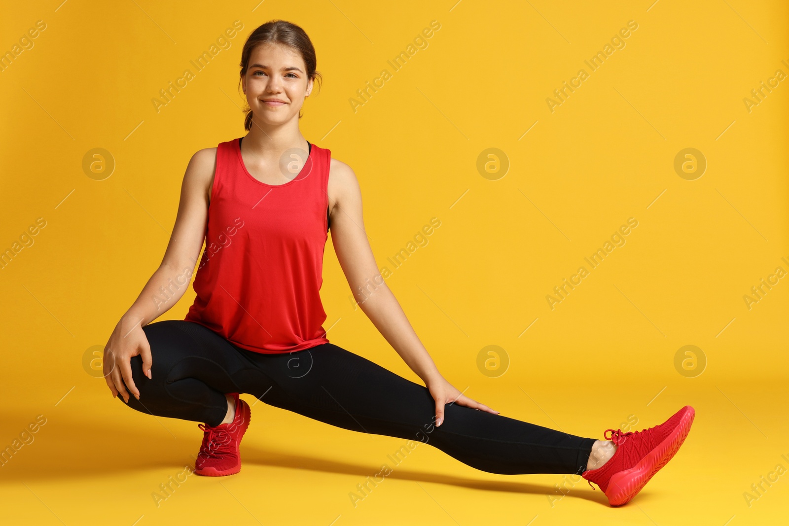 Teenage girl in sportswear stretching on orange background Photo of Teenage girl in sportswear stretching on orange background