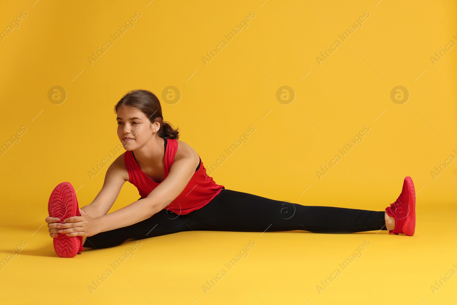 Teenage girl in sportswear stretching on orange background Photo of Teenage girl in sportswear stretching on orange background