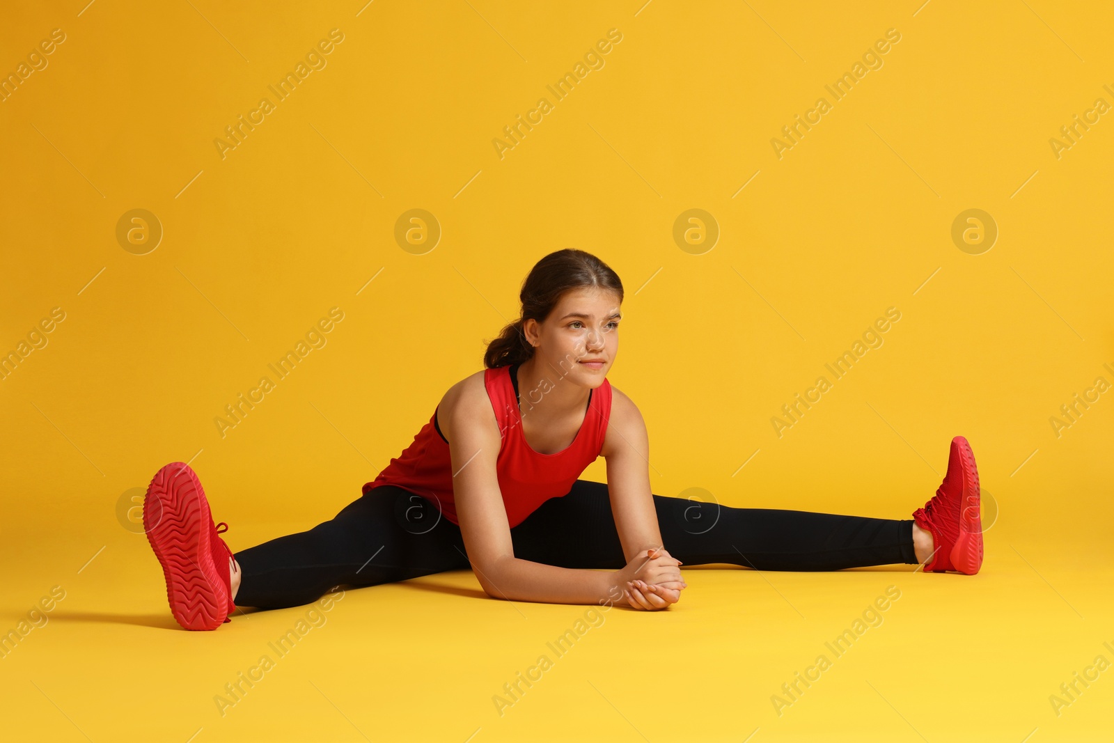 Teenage girl in sportswear stretching on orange background Photo of Teenage girl in sportswear stretching on orange background