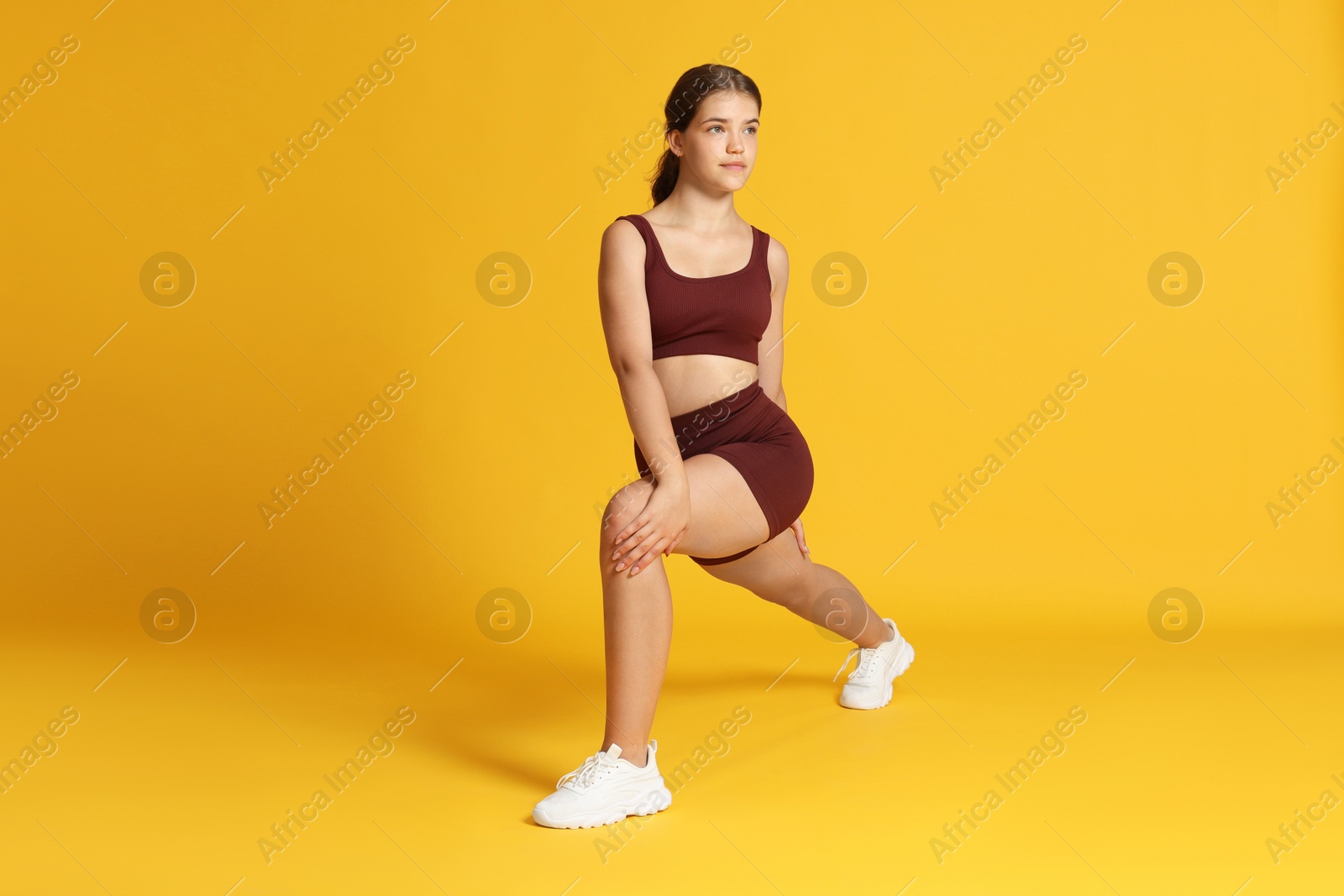 Teenage girl in sportswear stretching on orange background Photo of Teenage girl in sportswear stretching on orange background