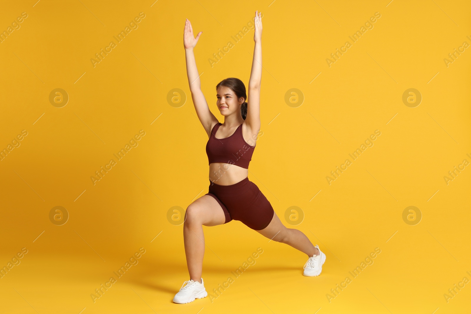 Teenage girl in sportswear stretching on orange background Photo of Teenage girl in sportswear stretching on orange background