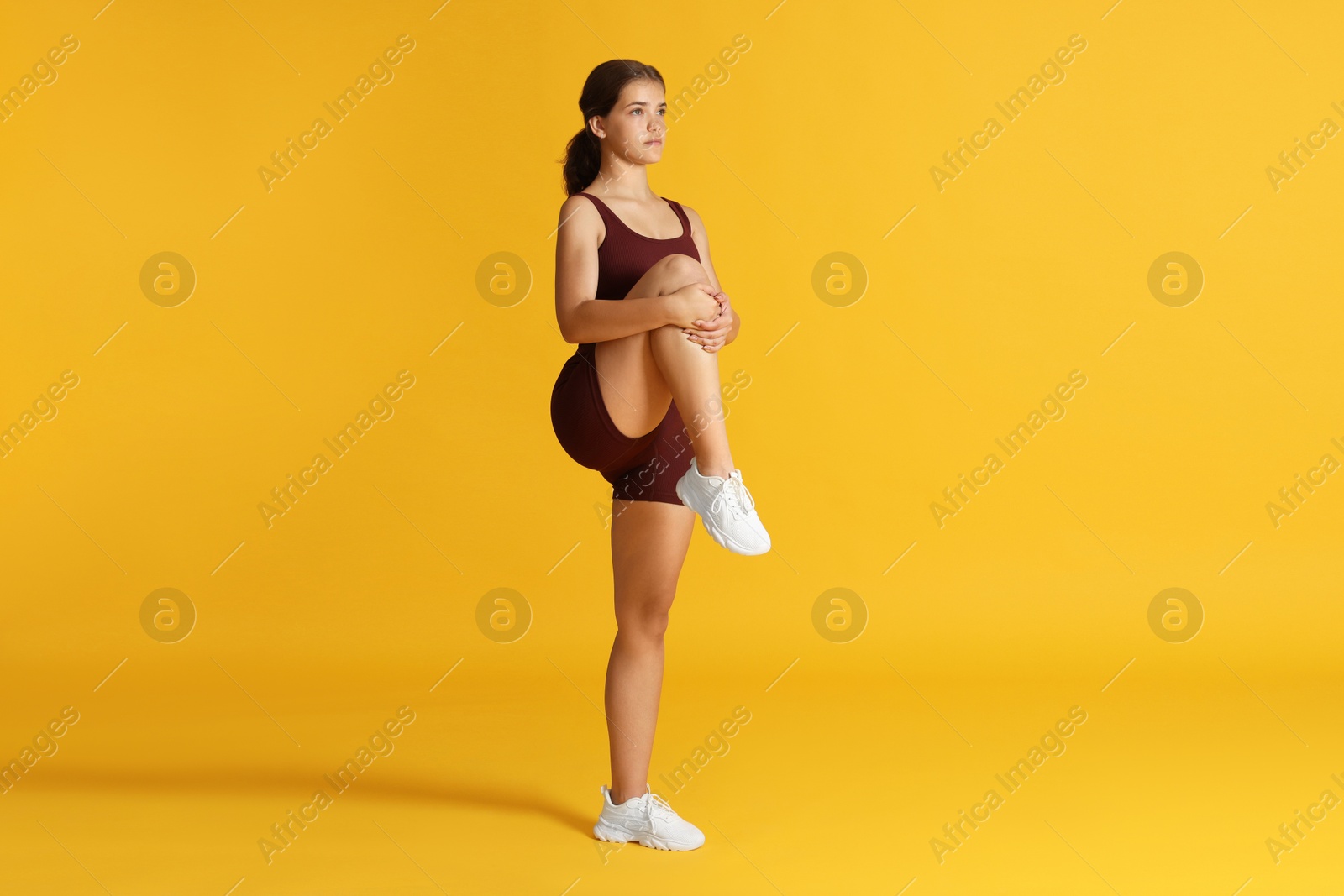 Teenage girl in sportswear stretching on orange background Photo of Teenage girl in sportswear stretching on orange background