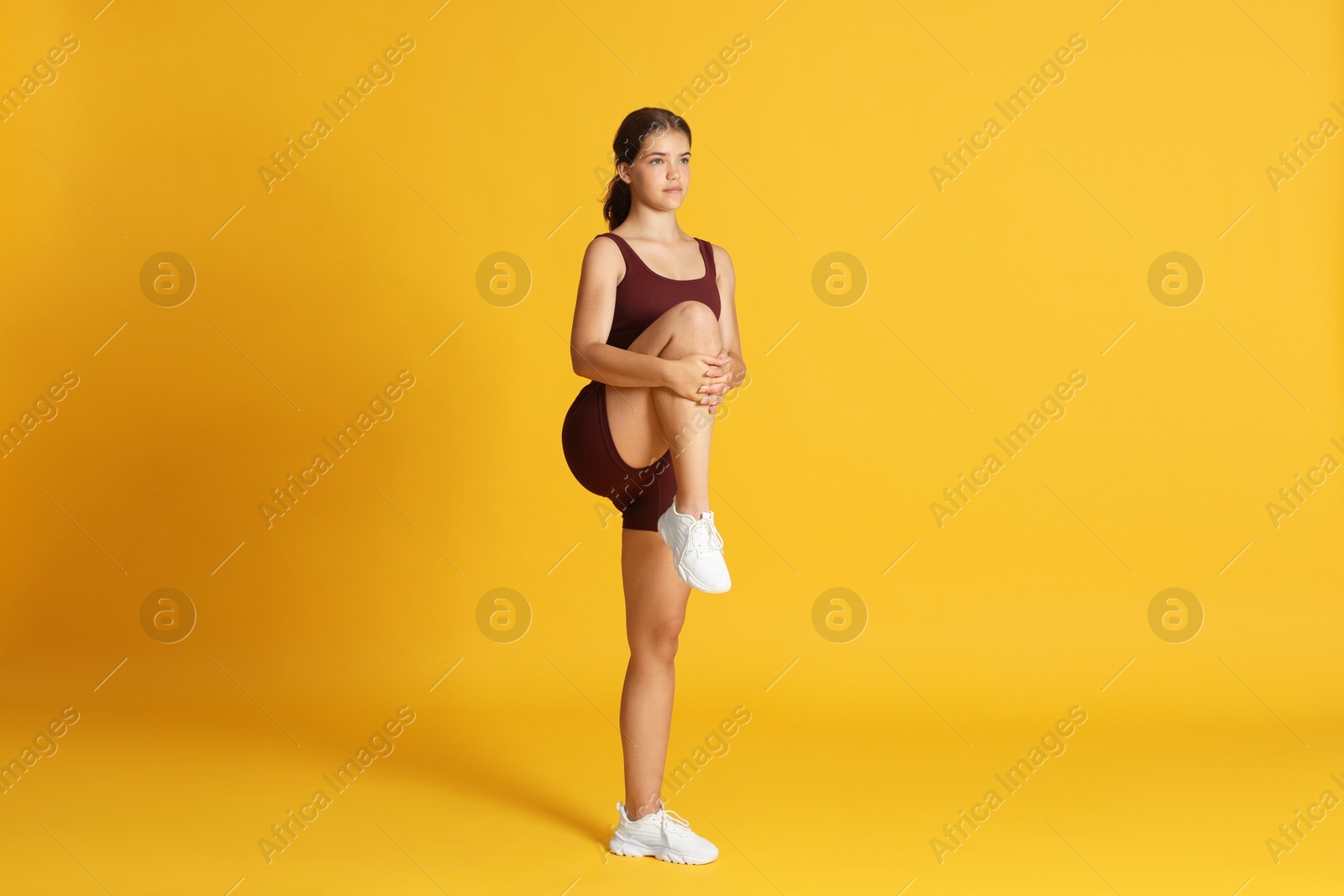 Teenage girl in sportswear stretching on orange background Photo of Teenage girl in sportswear stretching on orange background