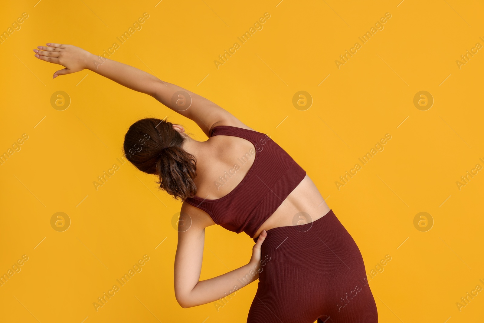 Teenage girl in sportswear stretching on orange background, back view Photo of Teenage girl in sportswear stretching on orange background, back view