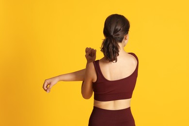 Photo of Teenage girl in sportswear stretching on orange background, back view