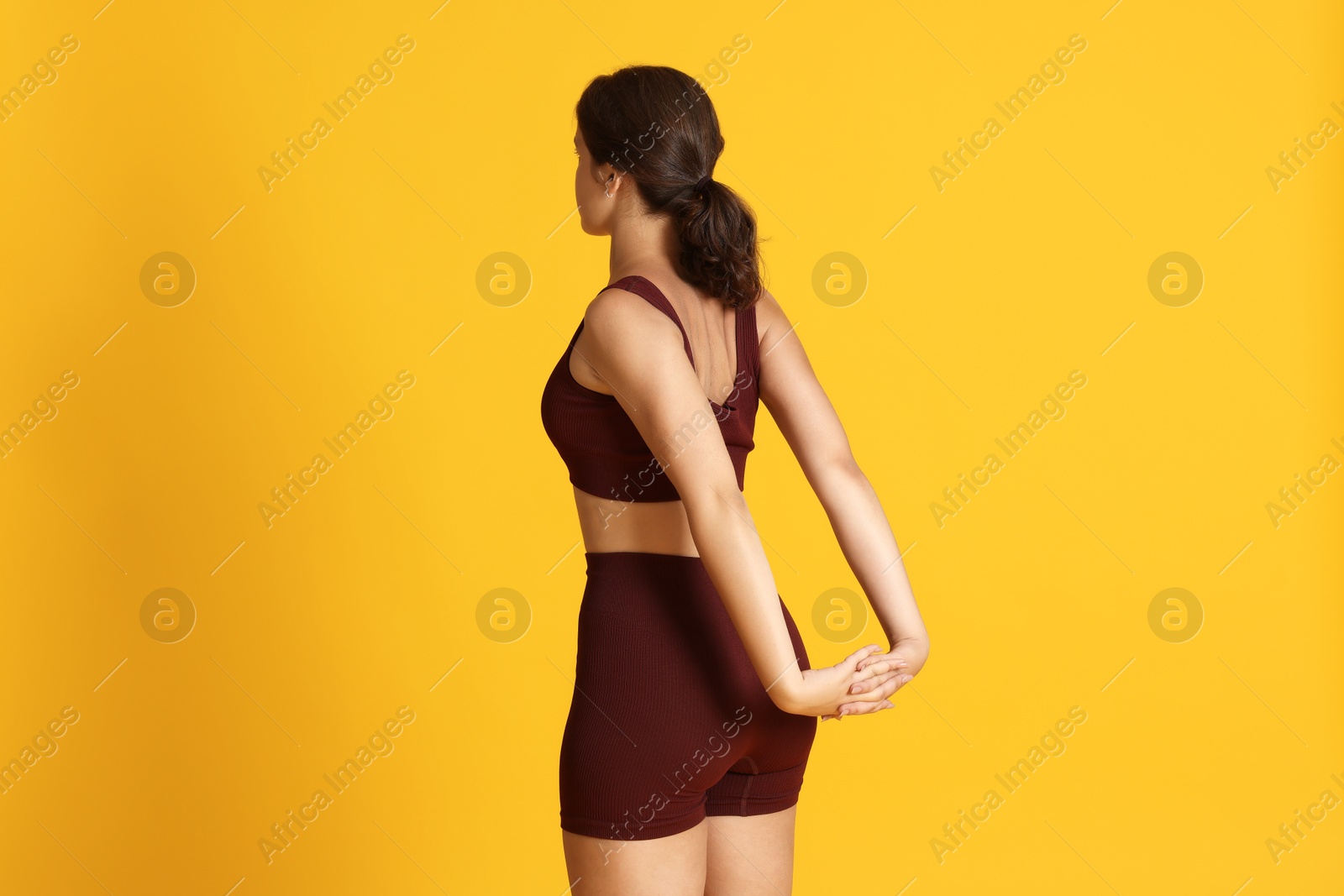 Teenage girl in sportswear stretching on orange background Photo of Teenage girl in sportswear stretching on orange background