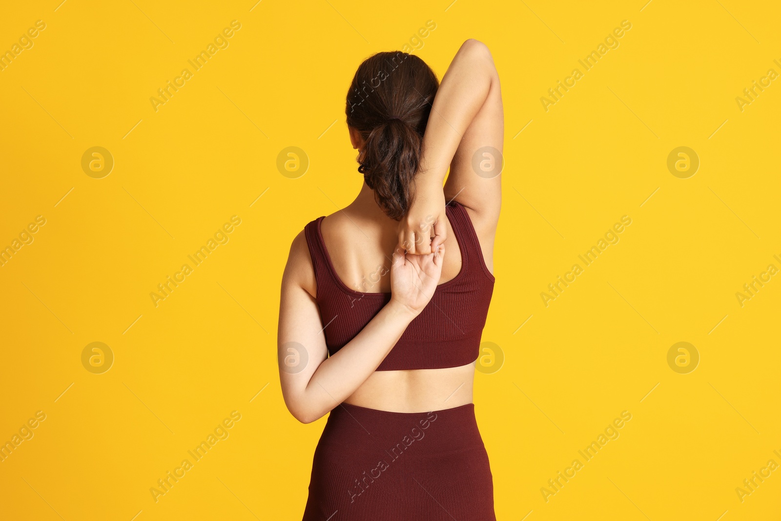 Teenage girl in sportswear stretching on orange background, back view Photo of Teenage girl in sportswear stretching on orange background, back view