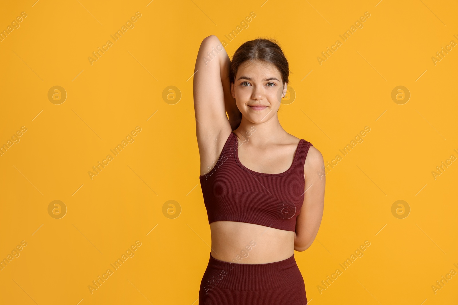 Teenage girl in sportswear stretching on orange background, space for text Photo of Teenage girl in sportswear stretching on orange background, space for text