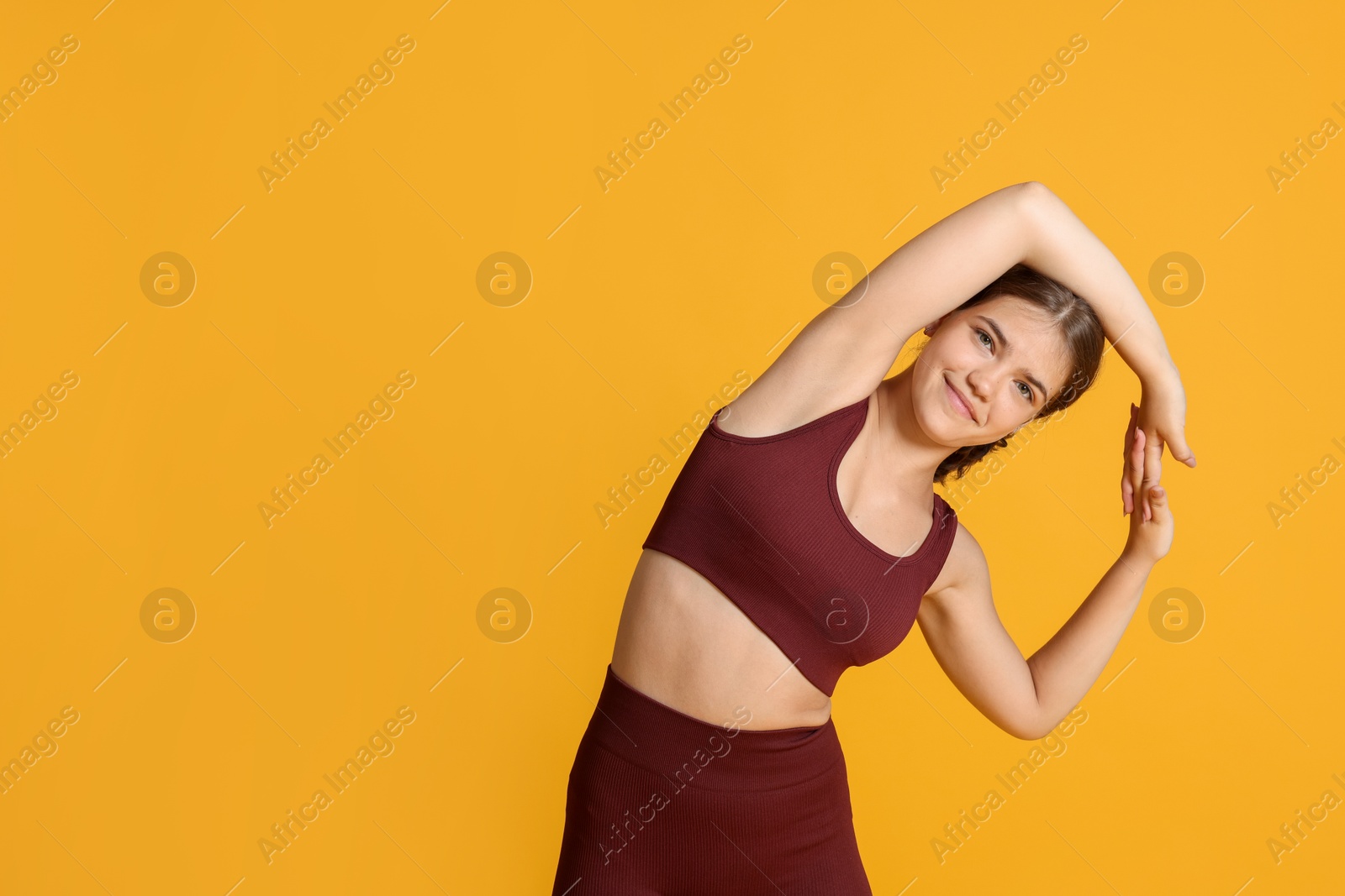 Teenage girl in sportswear stretching on orange background, space for text Photo of Teenage girl in sportswear stretching on orange background, space for text